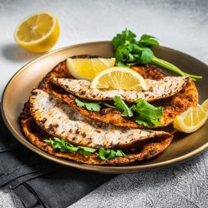 Turkish lahmacun pizza with mince meat and tomatoes on a plate with parsley and lemon.