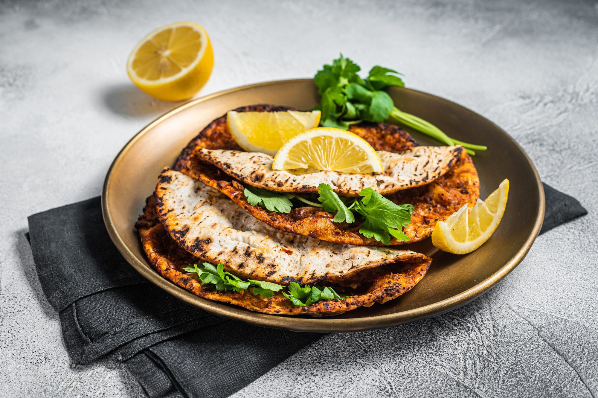 Turkish lahmacun pizza with mince meat and tomatoes on a plate with parsley and lemon.